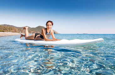 Young beautiful woman relaxing lying in the blue sea on a sup board near Chirali beach, Turkey