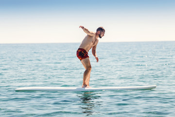 Beginner man try to surf on a board in a sea near the shoreline