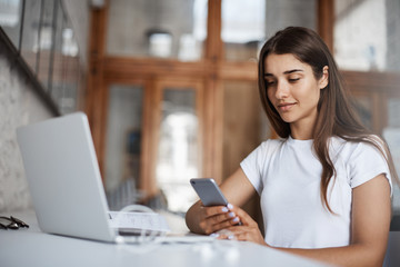 Young happy woman using a smart cell phone to look at her selfies to pick a new social media profile picture.