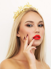 Beautiful stylish blonde girl with long wavy hair with a Golden crown on his head. Young Woman face portrait. Model with bright eyebrows, perfect make-up, red lips, touching her face. Sexy lady makeup