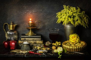 Classic still life with apple pie place with fresh apples,mussels,green olives,red chili, illuminated candle,drink and yellow flowers on marble background