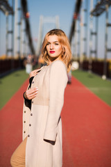 Street portrait of luxury blonde model wears fashionable apparel, posing at the bridge
