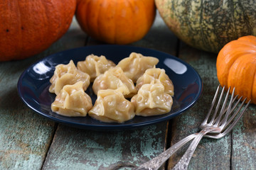 Traditional Asian dish, manti, steamed dumplings on navy blue plate served with raw pumpkins and vintage forks on shabby rustic table