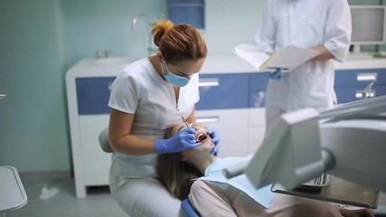 female dentist checking patient girl teeth. dentist with mirror checking patient girl teeth up at dental clinic office - Powered by Adobe