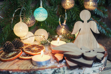 Wooden angel in front of a Christmas branch decorated with illuminated christmas balls