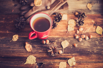 Hands in red knitted gloves holding a hot cup of coffee against yellow leaves background. Concept of autumn time, warmth and coziness