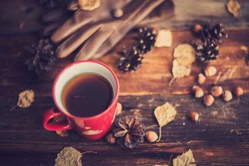 Hands in red knitted gloves holding a hot cup of coffee against yellow leaves background. Concept of autumn time, warmth and coziness