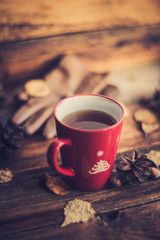 Hands in red knitted gloves holding a hot cup of coffee against yellow leaves background. Concept...