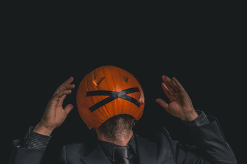 Man with a pumpkin head dressed in a suit against a black background