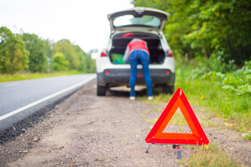A girl is climbing in the trunk of a car. Emergency sign near the car