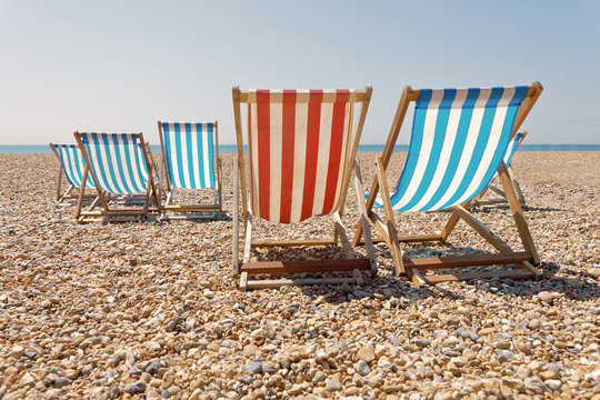 Peaceful day on the pepple beach, classic red and blue deckchairs, blue sea in the background