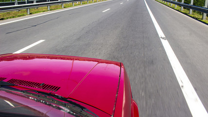 The red car rushes along the highway