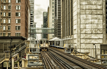 Fototapeta na wymiar Train on elevated tracks within buildings at the Loop, Glass and Steel bridge between buildings - Chicago City Center - Black Gold Artistic Effect - Chicago, Illinois, USA