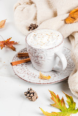 Obraz na płótnie Canvas Autumn hot drinks. Pumpkin latte with whipped cream, cinnamon and anise on a white marble table, with a sweater (blanket), autumn leaves and fir cones. Copy space