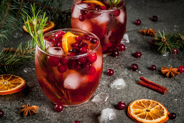 Christmas winter drinks. Cold cocktail with cranberries, orange, rosemary, with spices (cinnamon, anise) and ice, on a dark stone table, Copy space