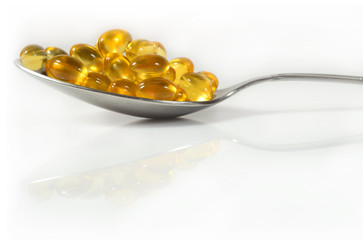 Omega-3 fish fat oil capsules in spoon on a white
