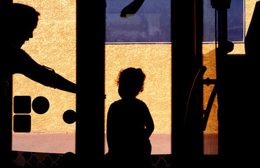 Black silhouettes of woman and little girl in the bus on the background of the yellow building wall
