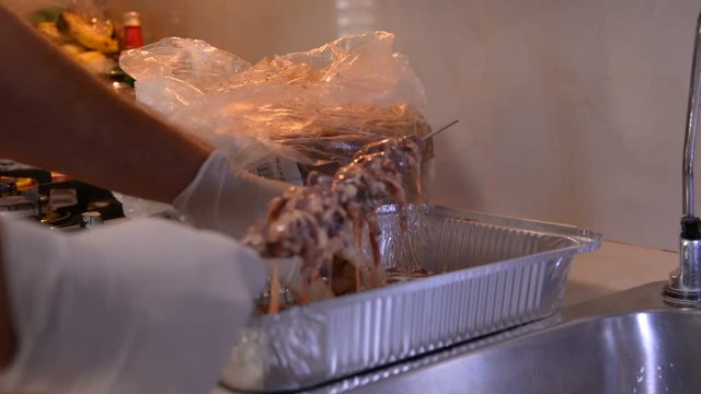 men hands in white gloves prepering raw chicken hearts for bbq on kitchen