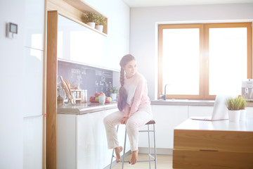 Young woman sitting on table in the kitchen.