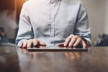 Closeup photo of male hands touching screen tablet. Modern tablet on large wooden table. Businessman typing text on tablet