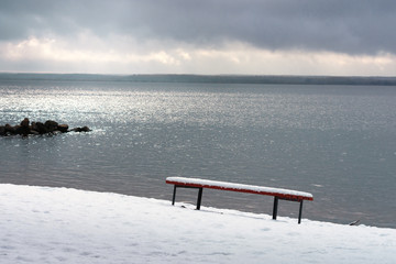 Park bench on the bank of the river, covered with heavy snow.