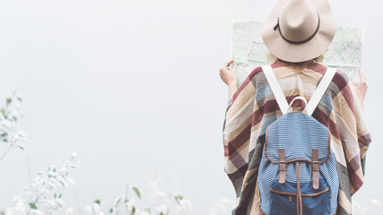 Young woman reading map in front of incredible mountain lake. Wearing hat, poncho and backpack....