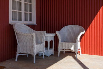 Two white wicker cane chairs on a veranda with red wall