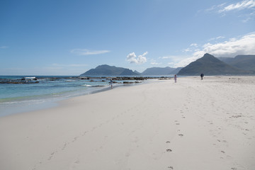 Three figures strolling on a pristine beach with mountains in background