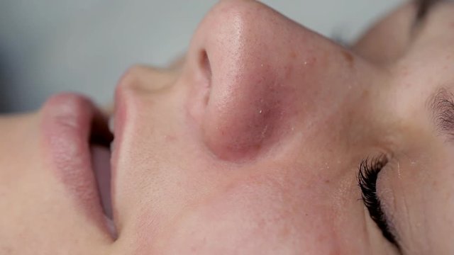 The beautician makes a cleansing of the nose area during the procedure of mechanical facial cleansing