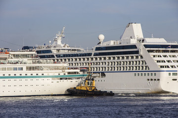 A huge cruise ships being manouvered and reversed towards high sea by pilots and tugboats