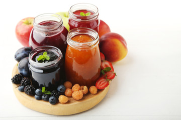 Glass jars with different kinds of jam and berries on wooden table