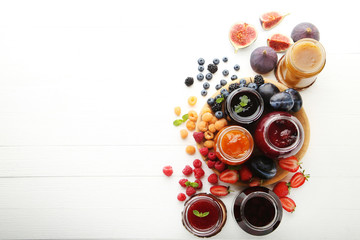 Glass jars with different kinds of jam and berries on wooden table - obrazy, fototapety, plakaty
