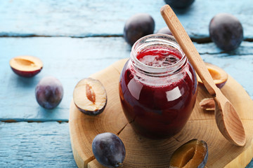Plum jam in glass jar with spoon on blue wooden table