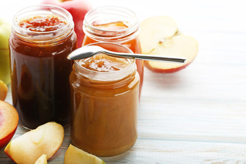 Apple jam in glass jars with spoon on white wooden table