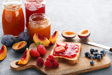 Bread with strawberry jam and ripe berries on grey wooden table