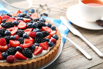 Sweet tart with berries in plate with cup of tea on grey wooden table