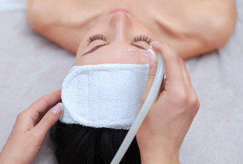 The cosmetologist makes the procedure vacuum face cleaning of a beautiful, young woman in a beauty...