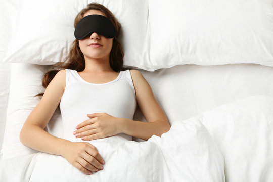 Young woman sleeping with eyemask in white bed
