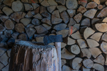 Iron axe on a tree stump, fire wood in the background