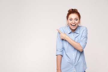 Wow! Handsome redhead woman in shoked. Pointing away while standing isolated on gray background - obrazy, fototapety, plakaty