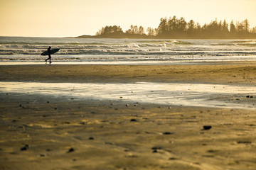 Fototapeta na wymiar A surfer walking along a golden sandy beach at sunset