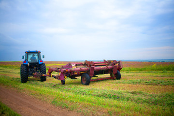 a tractor with a mower in the field of sainfoin and alfalfa mowing grass harvesting the field in summer