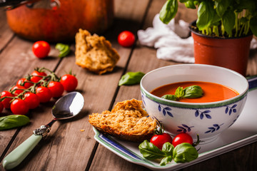 Tomato and basil soup shot on wood boards angled view with vine tomatoes loose basil spoon copper pot basil plant bread landscape