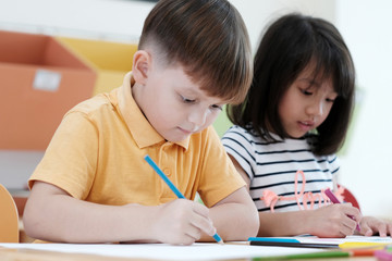 Boy and girl drawing color pencils in kindergarten classroom, preschool and kid education concept