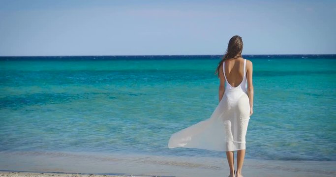Portrait of a woman stands on a wooden pier in a white dress, looks at the sea feels free, background of sea blue water and sky. Concept: freedom, beautiful sea view, slim body, vacation, light body.