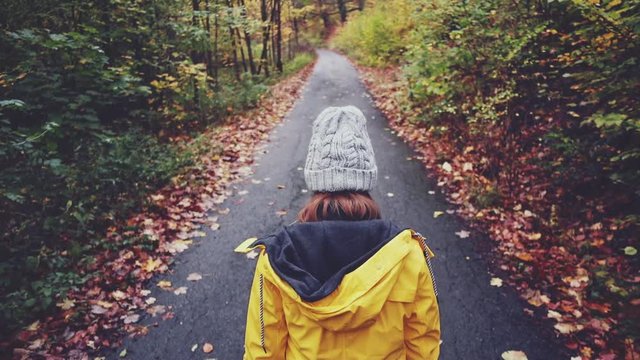 Woman Walking through Autumn Forest. SLOW MOTION 120 FPS, STABILIZED SHOT. Girl in yellow raincoat and knitted hat enjoying fall day outdoors, walking through woodland.  Disconnected concept. 