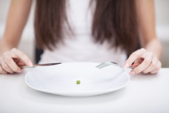 Diet. Suffering from anorexia. Cropped image of girl trying to put a pea on the fork