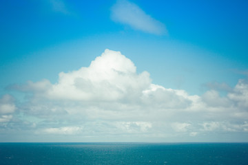 White cloud in blue sky above calm ocean water with copy space