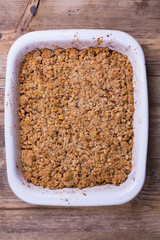 Apple crisp/crumble- a traditional fall dessert with apples. White baking dish and wooden background. 