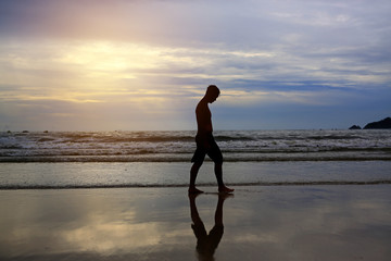 Man walking on the beach at sunset.